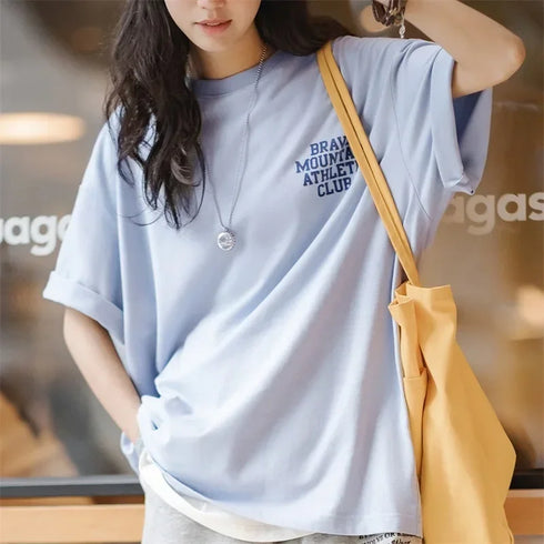 Person wearing a light blue t-shirt with text, holding a yellow bag indoors.